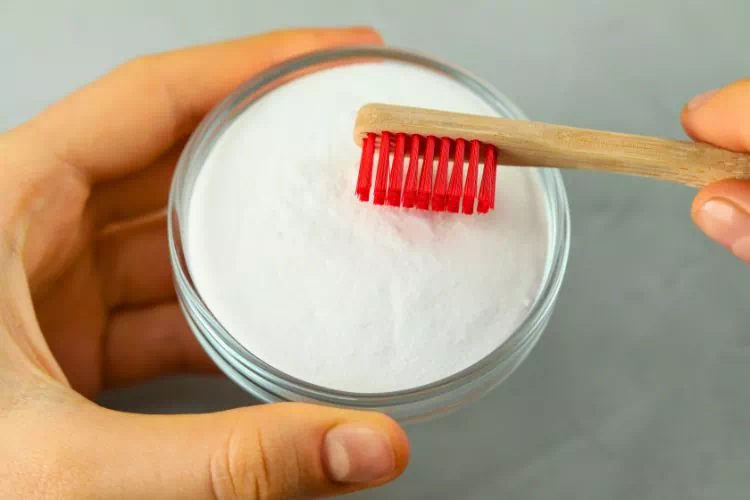 Personne mettant du bicarbonate sur sa brosse à dent